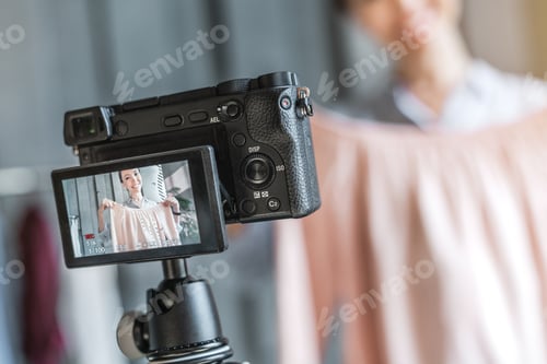 Preview: Close up of female fashion blogger showing cloth while recording vlog with camera at showroom