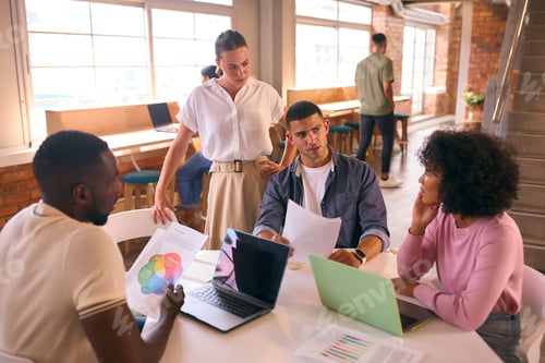 Preview: Multi-Cultural Business Team Meeting Around Desk In Modern Open Plan Office Discussing Documents