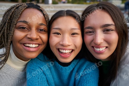 Preview: Cheerful close up portrait of three multiethnic female friends looking at camera with big smiles.