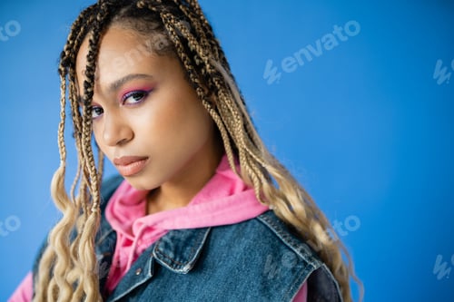 Preview: young african american woman with dreadlocks looking at camera on blue background, bold makeup