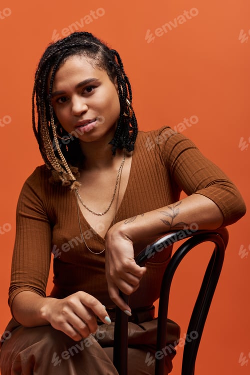 Preview: Stylish young African American woman with braided hair poses confidently in a vibrant studio