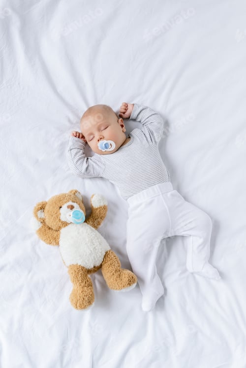 Preview: overhead view of cute baby with pacifier sleeping on bed with teddy bear
