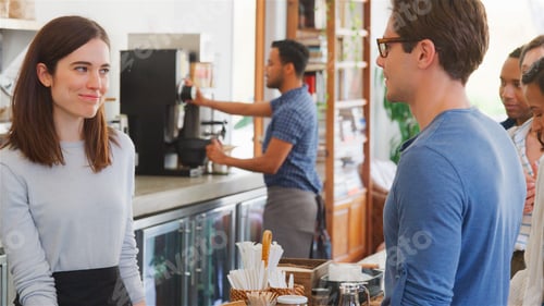 Preview: Female Worker Behind Counter Serving Male Customer In Busy Coffee Shop