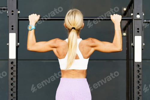 Preview: Strong woman doing pull ups on barbell in studio