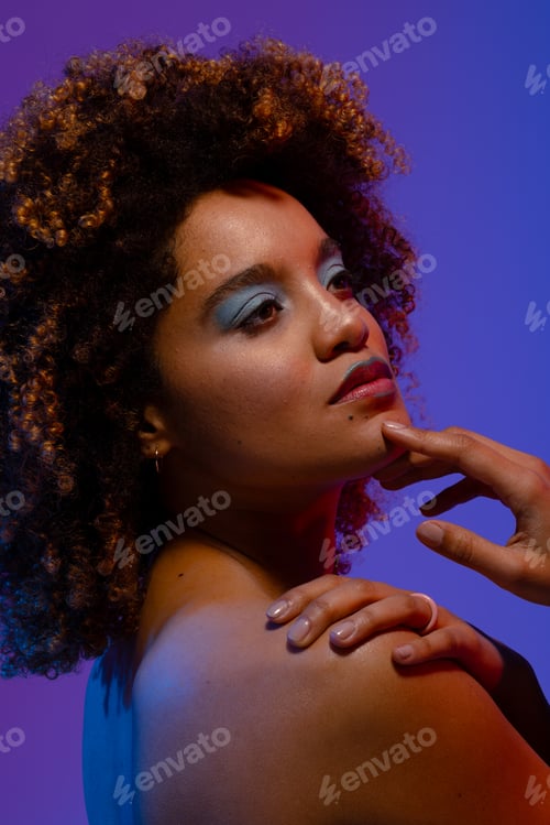 Preview: Biracial woman with curly hair and blue eye shadow with hand on chin and shoulder