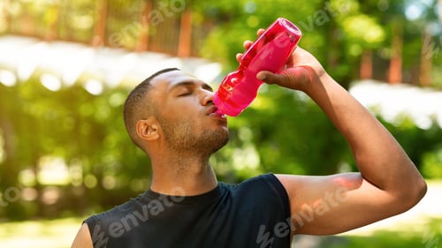 Preview: Thirsty black man drinking water from sports bottle after his training at park