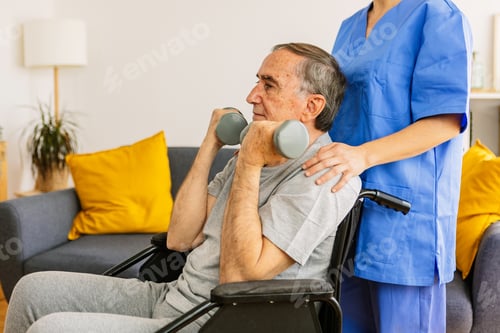 Preview: Old man in wheelchair training with physiotherapist using dumbbells at home.