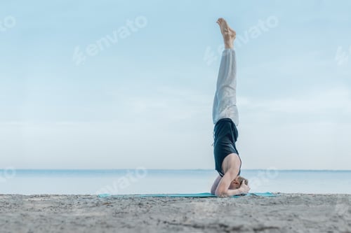 Preview: Young healthy man doing yoga exercises at the beach, balancing