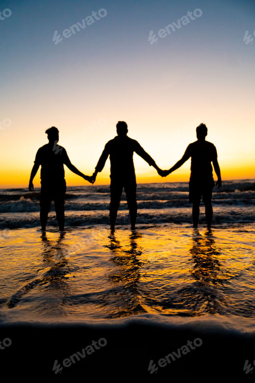 Preview: Three people standing with hands linked in a line at the beach on a sunny evening