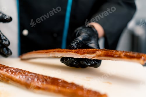 Preview: Close-up of a sushi chef in gloves cutting an eel fillet with a professional knife on kitchen table
