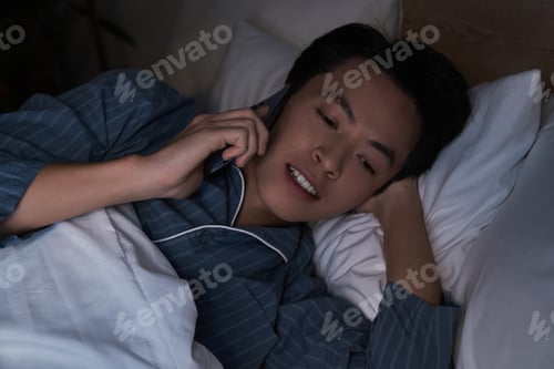 Preview: Asian man having phone conversation in a cozy modern apartment at night