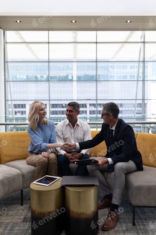 Preview: Caucasians business executives shaking hand while sitting on the sofa in modern office.