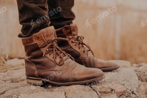 Preview: Man in brown old leather boots and trousers stands on stones against blurred background.