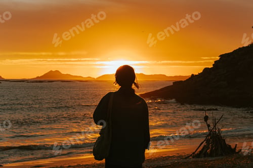 Preview: A traveler in front of a colorful sunset in the beach wearing a face mask, wellness concept,
