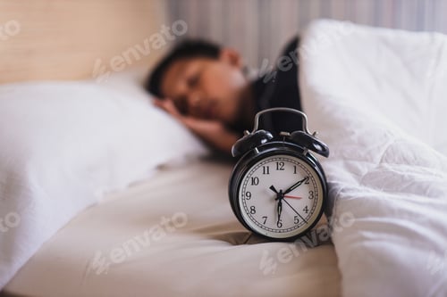 Preview: Alarm clock beside the bed and young sleeping boy.