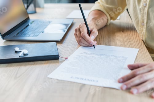 Preview: Cropped view of businessman writing on blurred contract near notebook and earphones on table