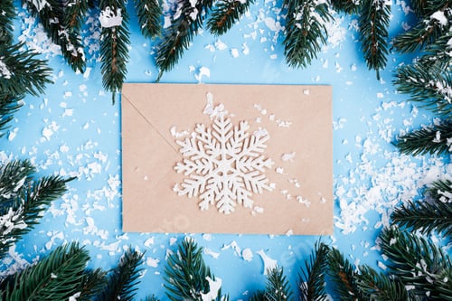 Top view of envelope, decorative snowflake and pine branches with artificial snow on blue background