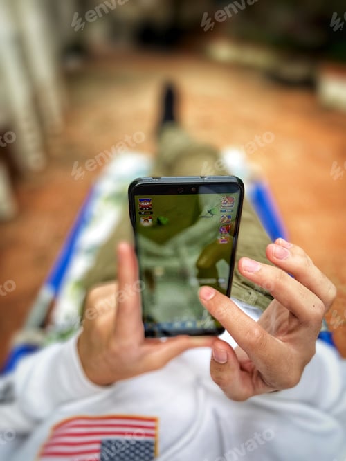 Preview: Young millenial boy playing with mobile phone relaxing on spring day