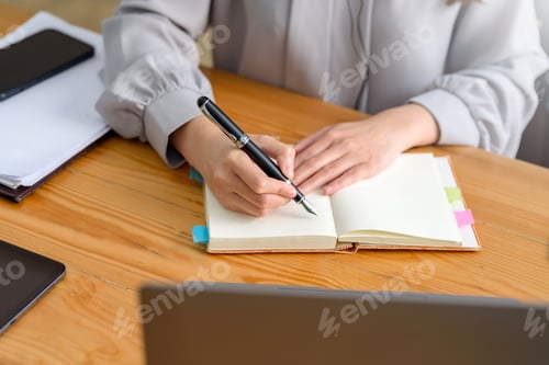 Preview: Close up image of a woman writing and taking note on notebook with laptop in office.