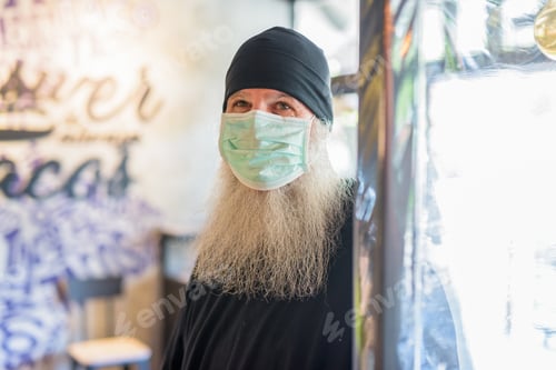 Preview: Mature bearded hipster man wearing mask as the new normal inside the coffee shop