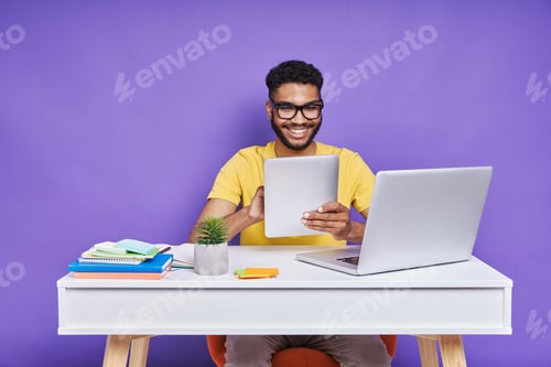 Preview: Confident African man using digital tablet while sitting at the desk against purple background