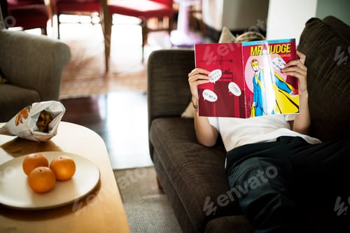 Preview: Young caucasian man lying on the couch reading cartoon