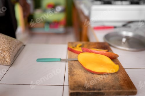 Preview: Some pieces of mango are chopped on the cutting board next to a blue knife.