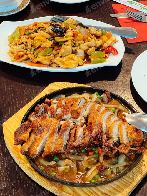 Preview: Sweet and sour chicken and Sichuan duck stand on plates on a table in a restaurant