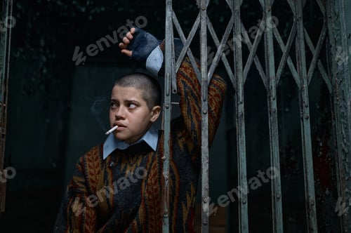 Preview: Unhappy depressed woman beggar with smoldering cigarette behind bars