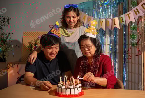 Preview: A woman is cutting a birthday cake with candles while two other people look on