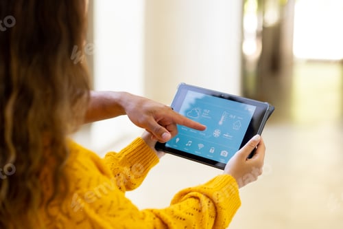 Preview: Diverse couple at home, woman holding tablet and man pointing to smart home interface on screen