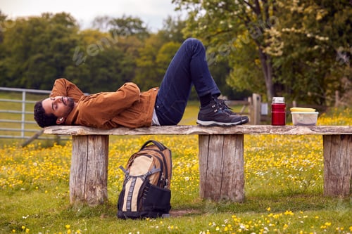 Preview: Man Lying On Bench In Countryside Relaxing And Listening To Music Or Podcast On Wireless Earphones