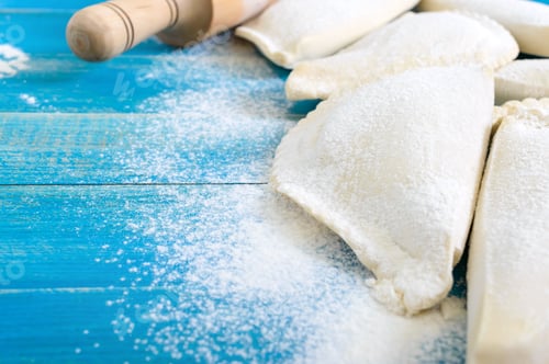 Preview: Not fried chebureks in flour on a blue wooden table.