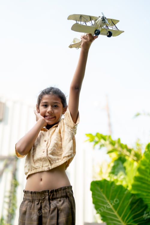 Preview: Asian girl enjoy to play with plane model in home garden or yard with warm light and blue sky