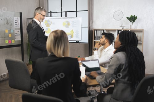 Preview: Multiethnic investors, sitting at the table in office while handsome middle aged male manager