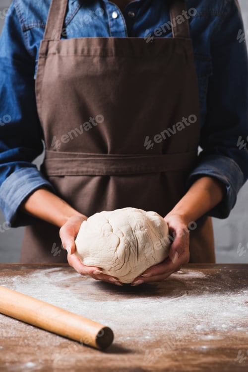 Preview: cropped shot of woman in apron holding raw dough for pizza in hands