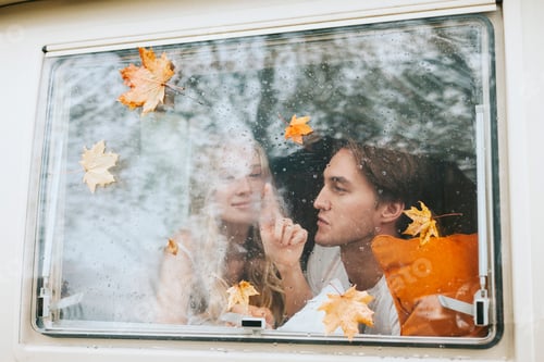 Preview: couple in love from window with rain drops and autumn leaves having fun together, young man and woma