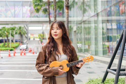 Preview: Young woman happy person travel tourist enjoys holiday music, playing ukulele outdoors on vibrant