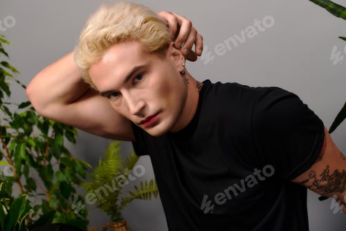 Preview: Stylish young man posing confidently in a modern indoor setting surrounded by greenery