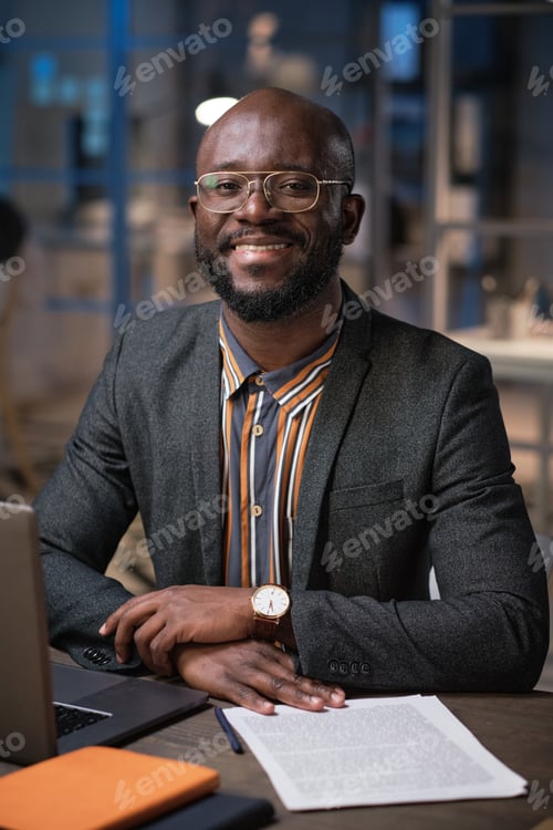 Preview: Portrait of African manager smiling at camera while working at his table with business documents