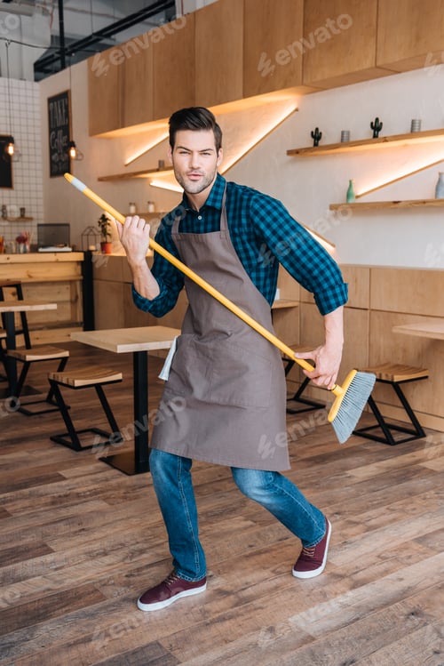 Preview: playful man pretending playing guitar with broom in cafe