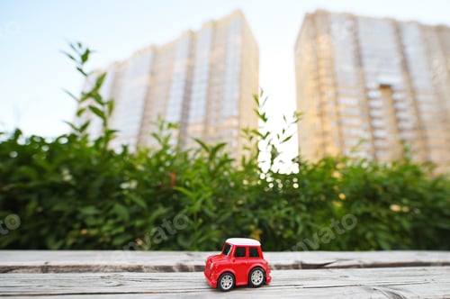 Preview: toy red car on the background of new buildings and greenery