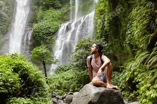 Preview: Nature, tourism and people. Young barefooted tourist wearing jeans short and backpack sitting on big