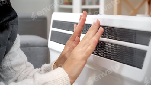 Preview: Closeup of woman warming hands at electric heater or radiator. Concept of energy crisis, high bills