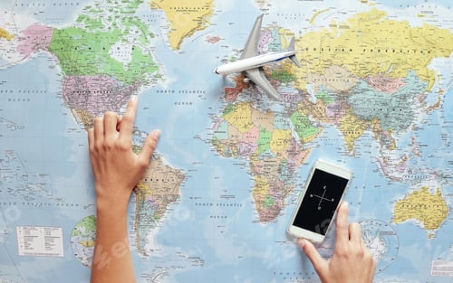 Preview: Top view of young tourist woman pointing her next travel destination using world map and phone