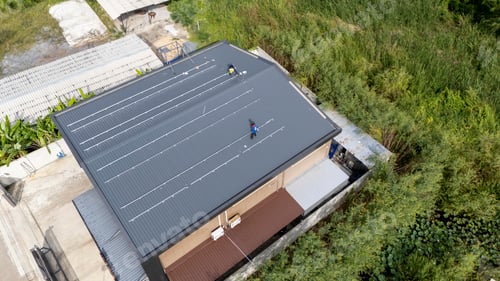 Preview: Workers installing a new roof on a building surrounded by greenery in daylight