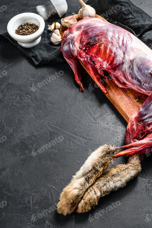 Preview: Whole forest farm hare, raw meat on wooden deck, old black rustic table. top view