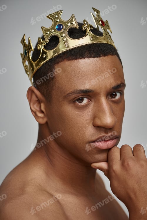 Preview: alluring african american man in golden crown posing topless with hand near face, fashion concept