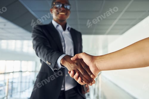 Preview: Doing handshake with customer. Young african american businessman in black suit is indoors