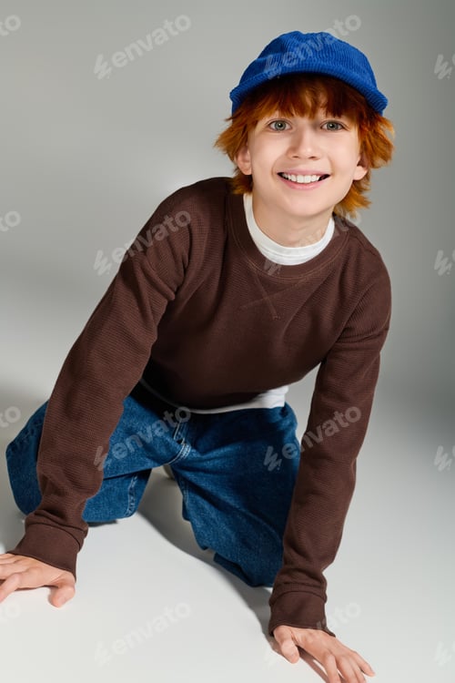 Preview: Bright and cheerful redhead boy poses in stylish casual wear in a modern studio
